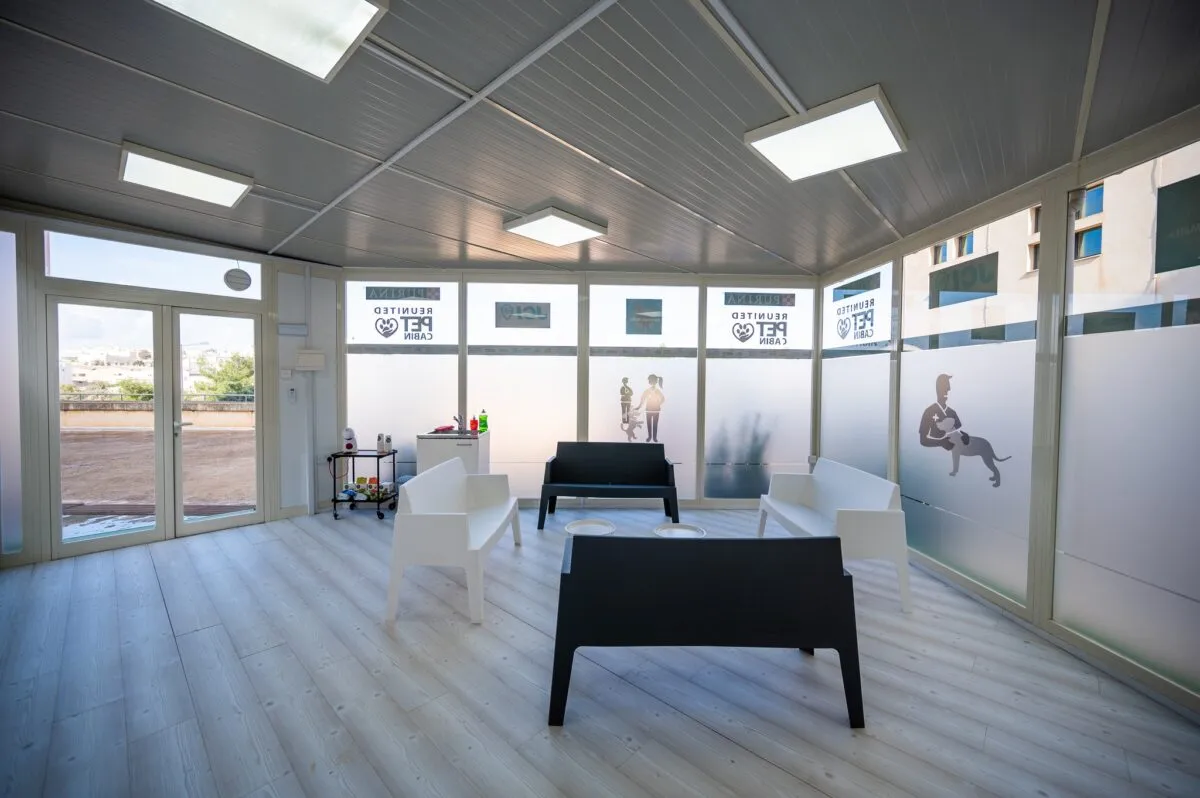 Inside the finished Reunited Pet Cabin: a bright room with white floors, armchairs and Reunited Pet Cabin signage on the glass